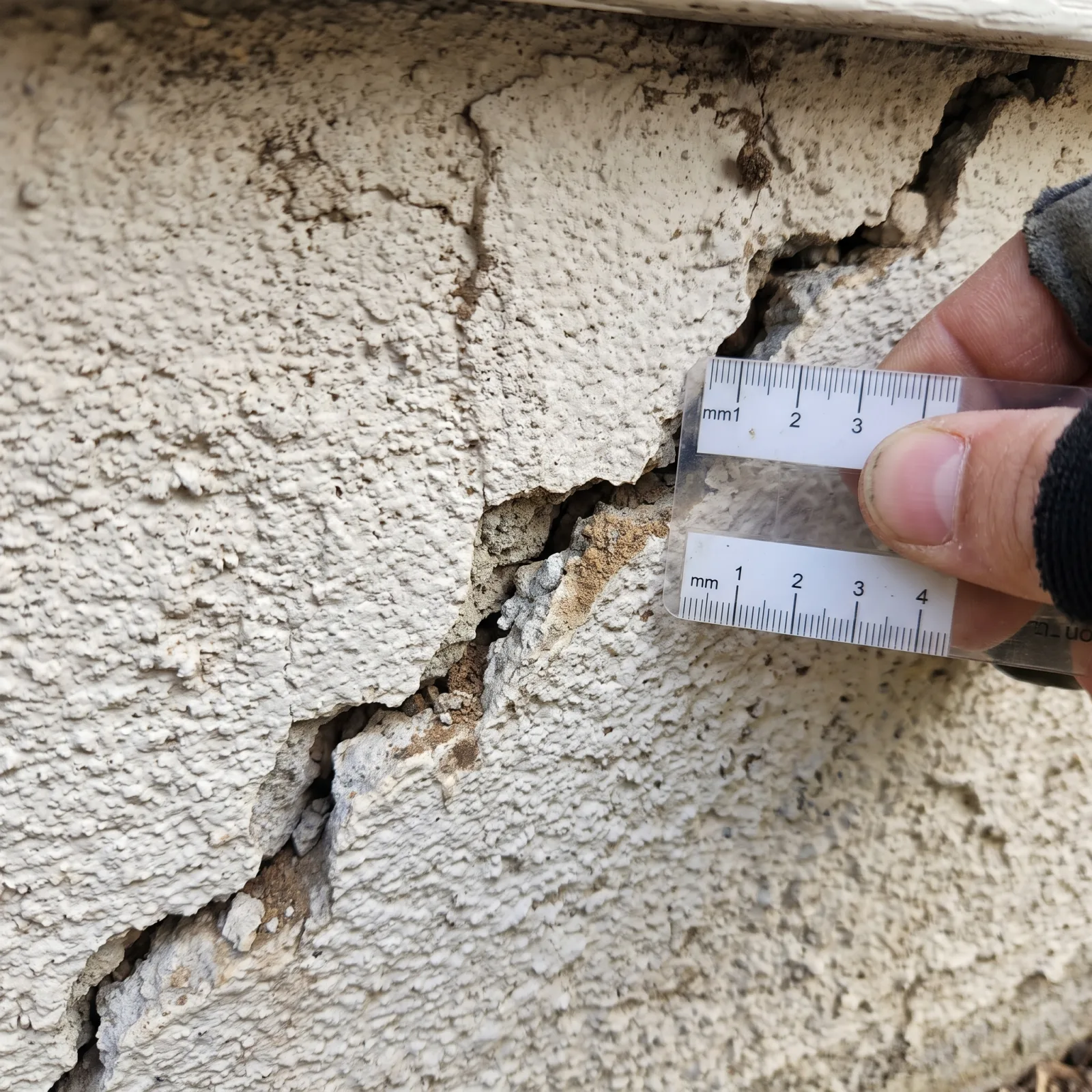 Close-up of a diagonal stucco foundation crack being measured with a crack-width card